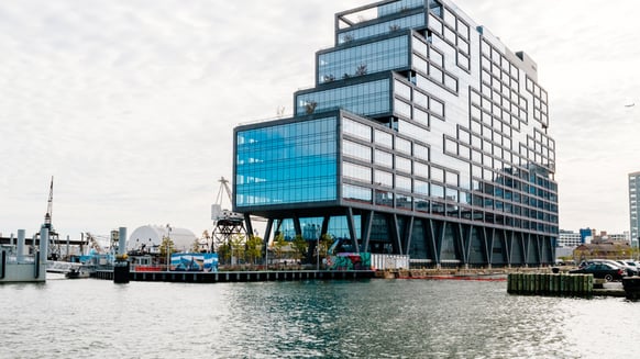 An image of the Dock 72 building as seen from the water. The frontage is mainly glass with a metal frame with a terraced layout.